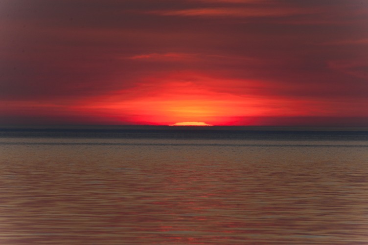 A red sun setting over the water. 