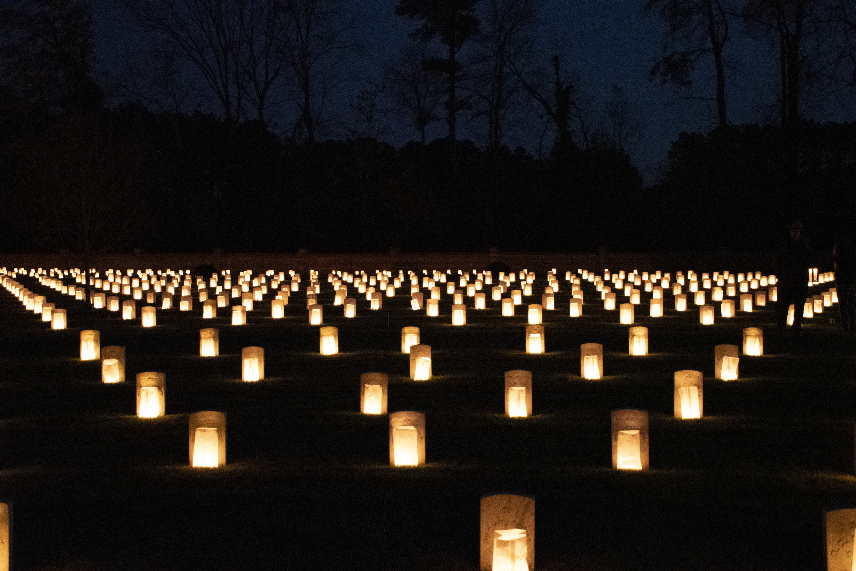 Hundreds of luminaries in front of headstones light up the night. 