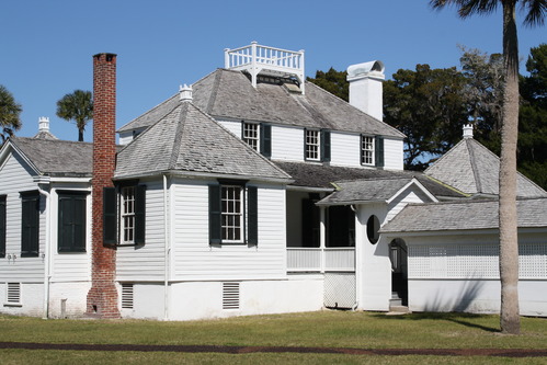 a two story white historic building with black shutters and a red brick fireplace to the side, a breeze way is attached at the center of the porch