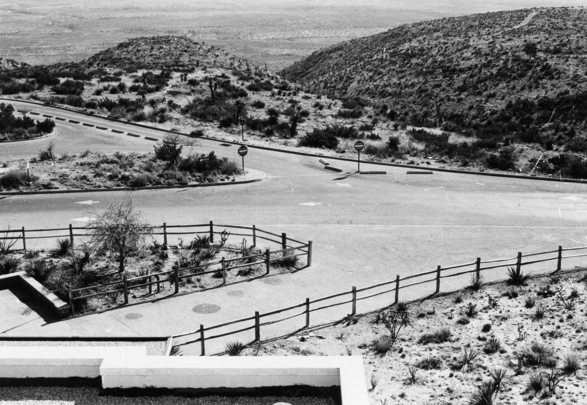 A black and white photograph of the road into and out of the visitor center parking lot taken from the roof of the visitor center.