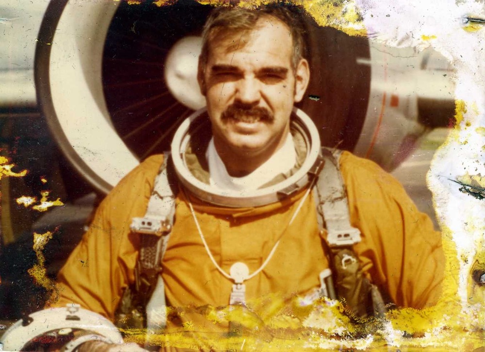 a man in a pressurized suit standing in front of an airplane