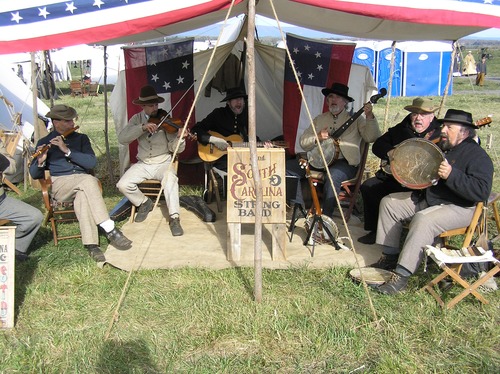 Several reenactors playing flute, fiddle, guitar, banjos and a large tambourine