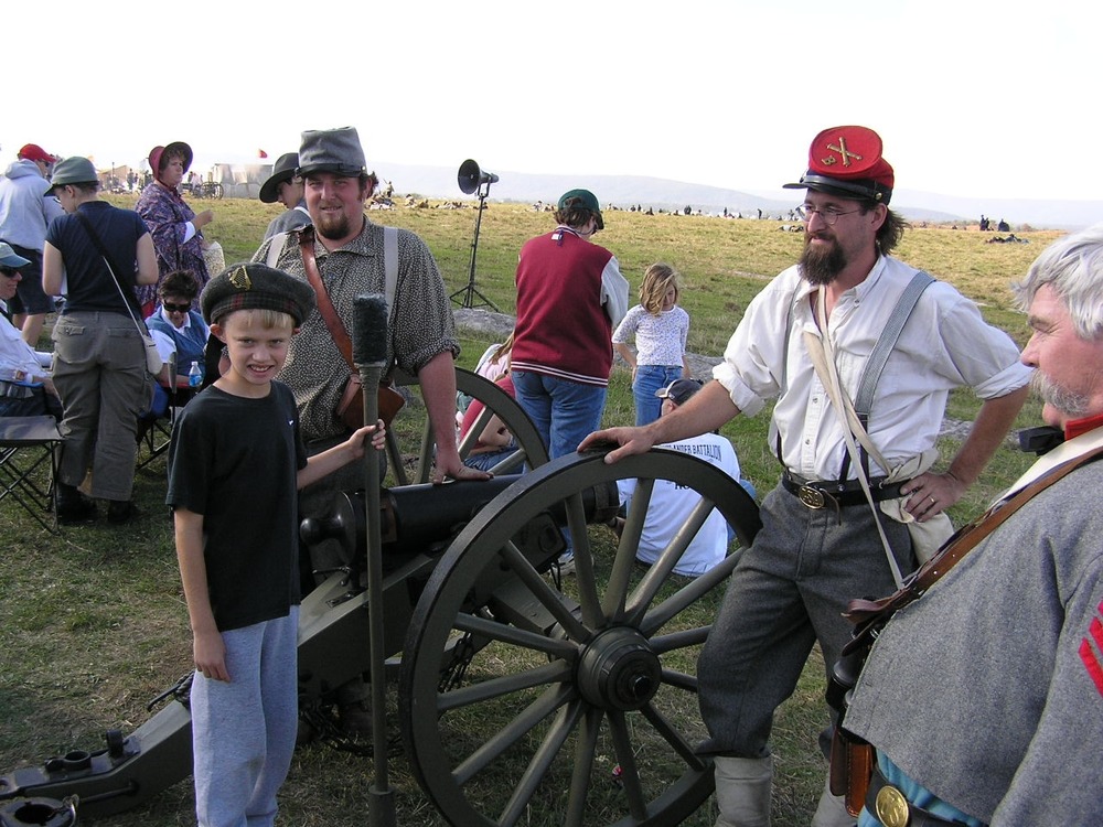 A young boy talks with a few Southern artillery soldiers as they explain how Civil War cannons were loaded and fired.