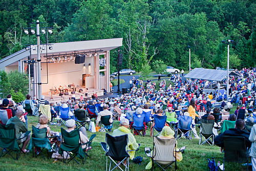 Amphitheater with a large crown enjoying music, in front of a forested background. 