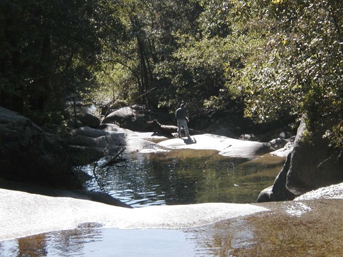 A person fishes in the distances, standing among pools of water in the rocks.