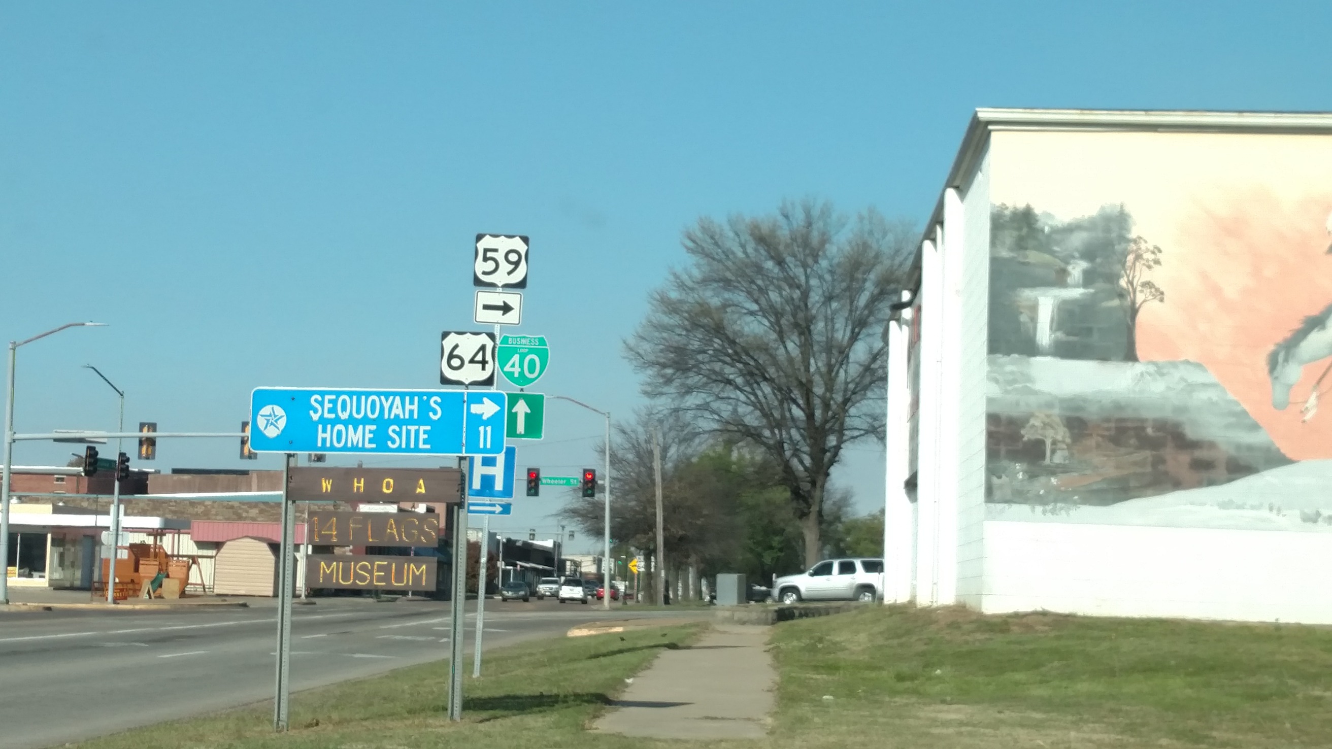 
A street view with road signs, a sidewalk, and a building with a mural, under a clear sky.