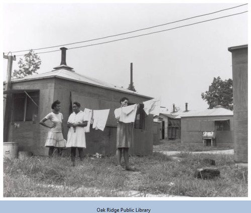 Three African American women hang up laundry outside a low square building.