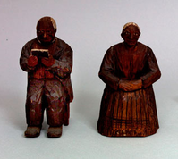 Two small hand carved wooden figurines, one a man reading a book, the other a woman with hands in her lap. 