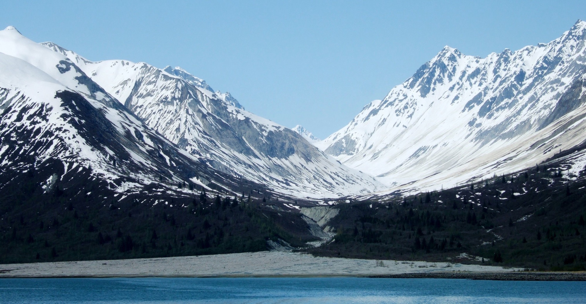 snowy mountains form a u shape with a blue bay in the foreground