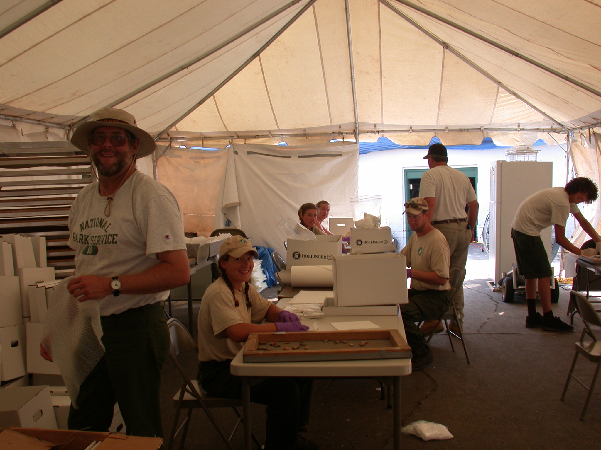 A group of people in at folding tables in a temporary tent working.