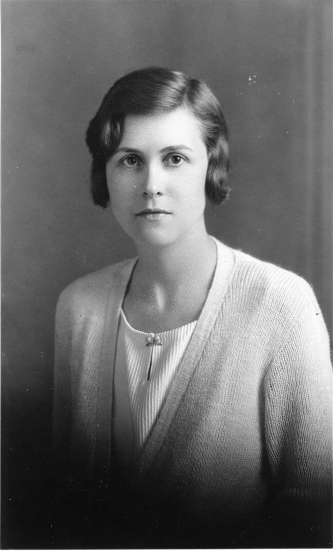 Woman in pale sweater over a white blouse looks intently at the camera in a black and white image.