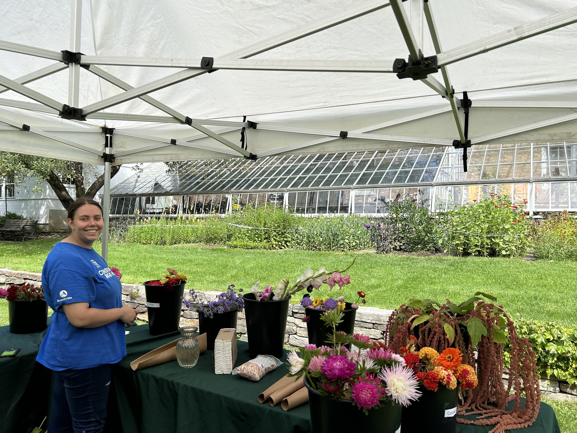 Park employee in blue shirt smiles at camera next to table with buckets of cut flowers