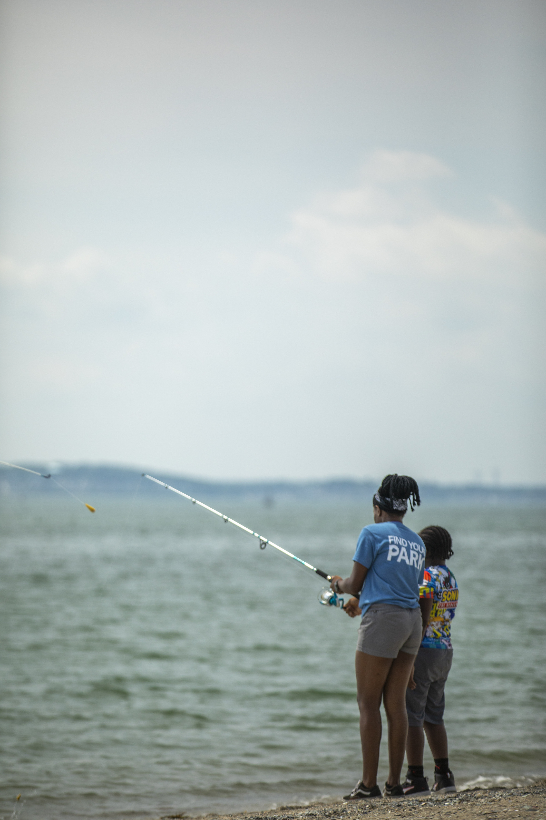 Two people holding a fishing pole on shoreline.