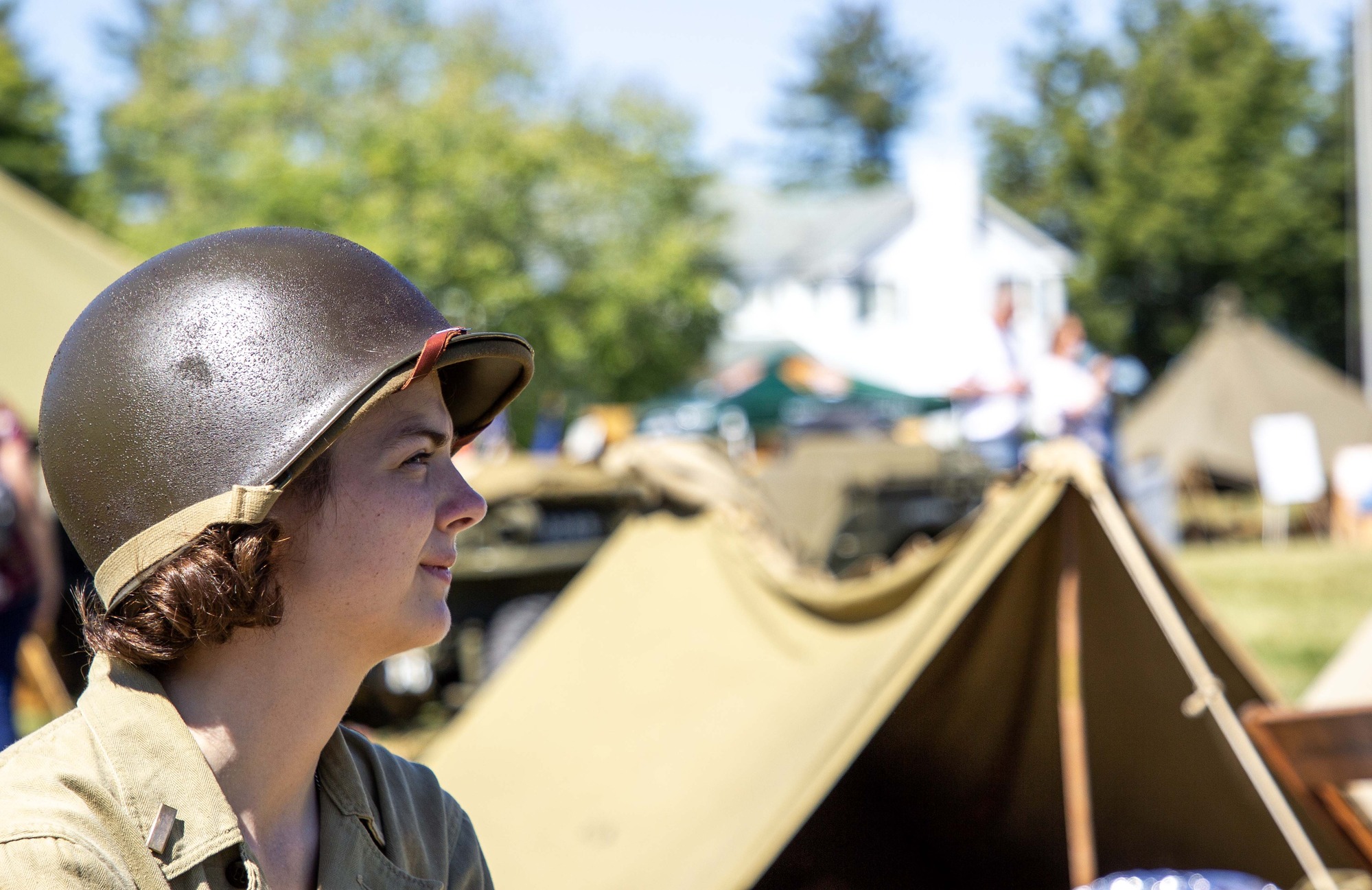 A living history volunteer with a green army helmet in front of green tents