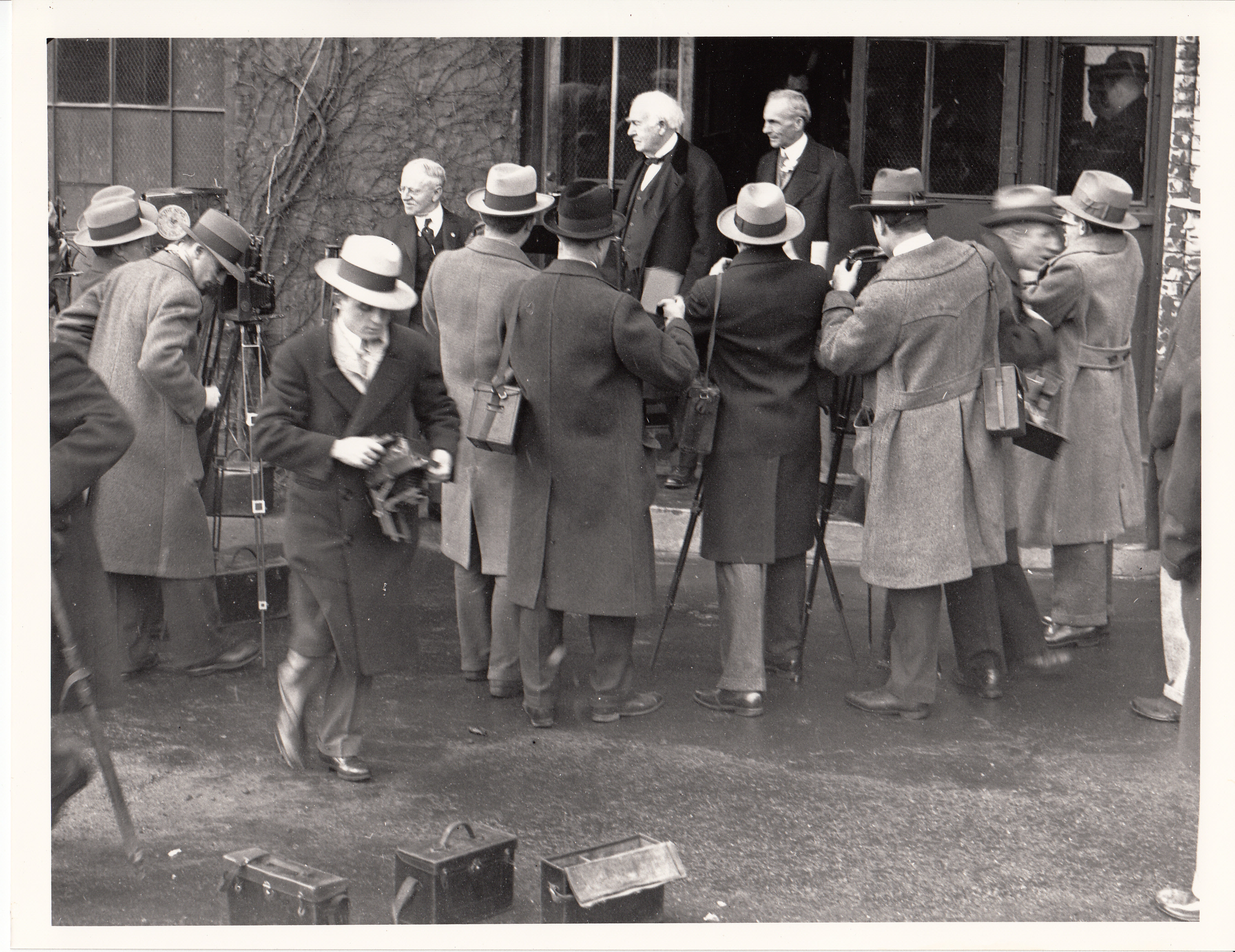 Thomas Edison greeting photographers in doorway of Building 5 on his eightieth birthday, W.H. Meadowcroft at left, Henry Ford at right.
