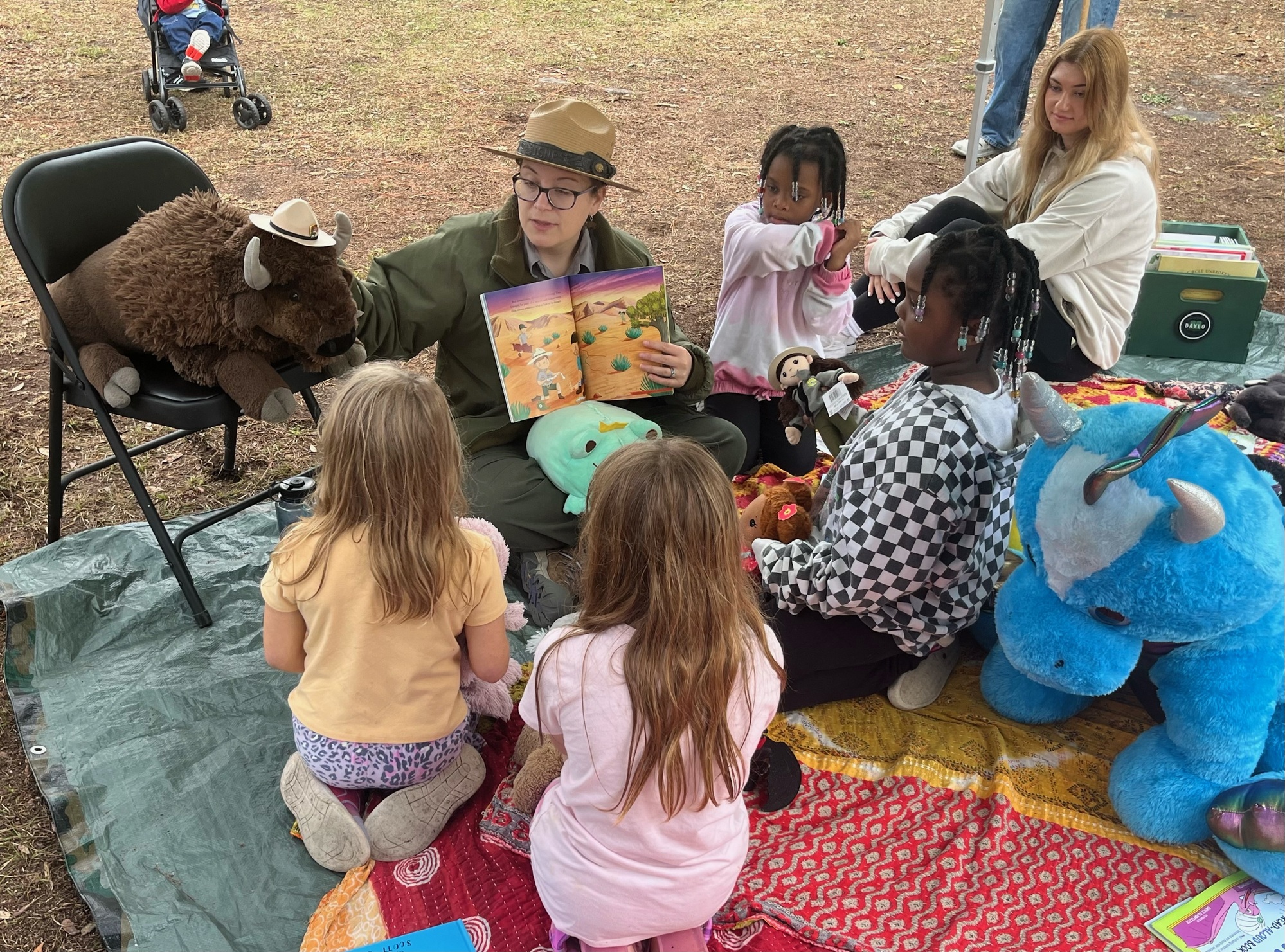 A ranger reads to a group of children surrounded by stuffed animals.