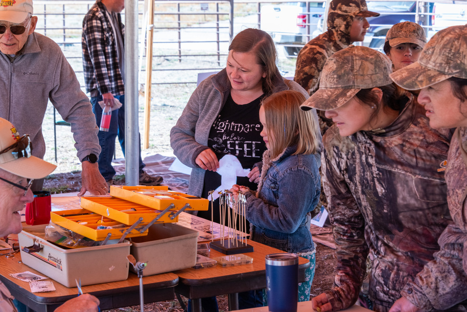 A large group of hunters wearing camouflage gathers around a fly tying booth.