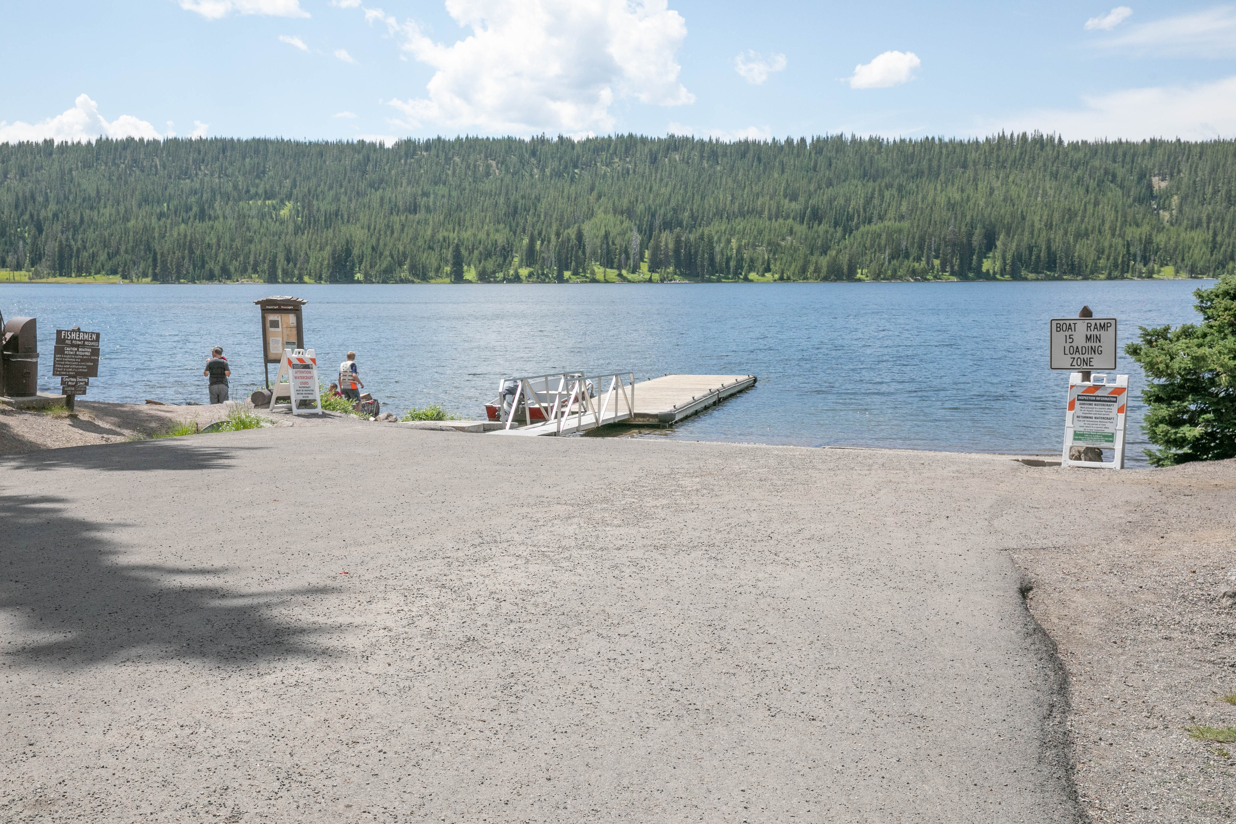 Asphalt road leads to the lake with a dock to the left.