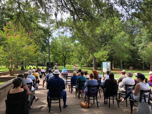 An audience is seated in chairs as park rangers speak in the visitor center plaza.