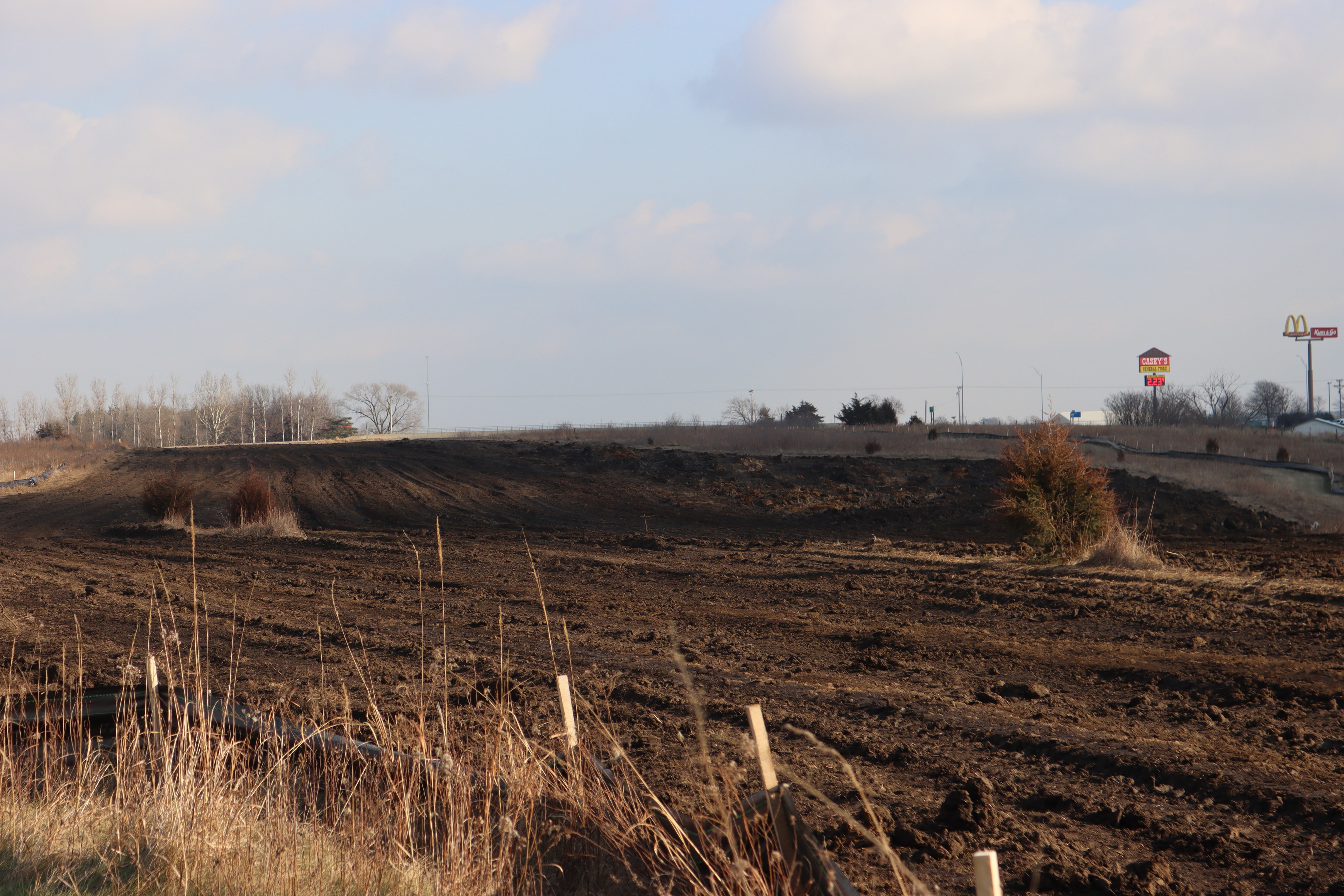 A large strip of disturbed dirt stripped of vegetation fills much of the frame. Remnants of the surrounding prairie grasses pop up in the foreground and on each side in the distance.
