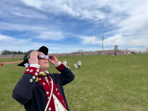 A man dressed in Continental Soldiers gear looks up at the sky with special tinted glasses. 