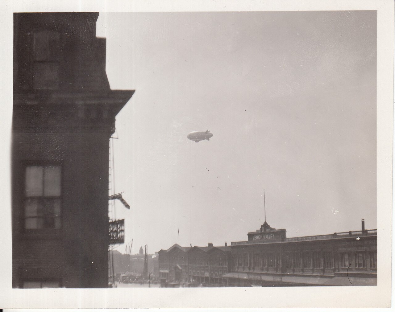Airship in flight above building which has sign marked, "Lehigh Valley."