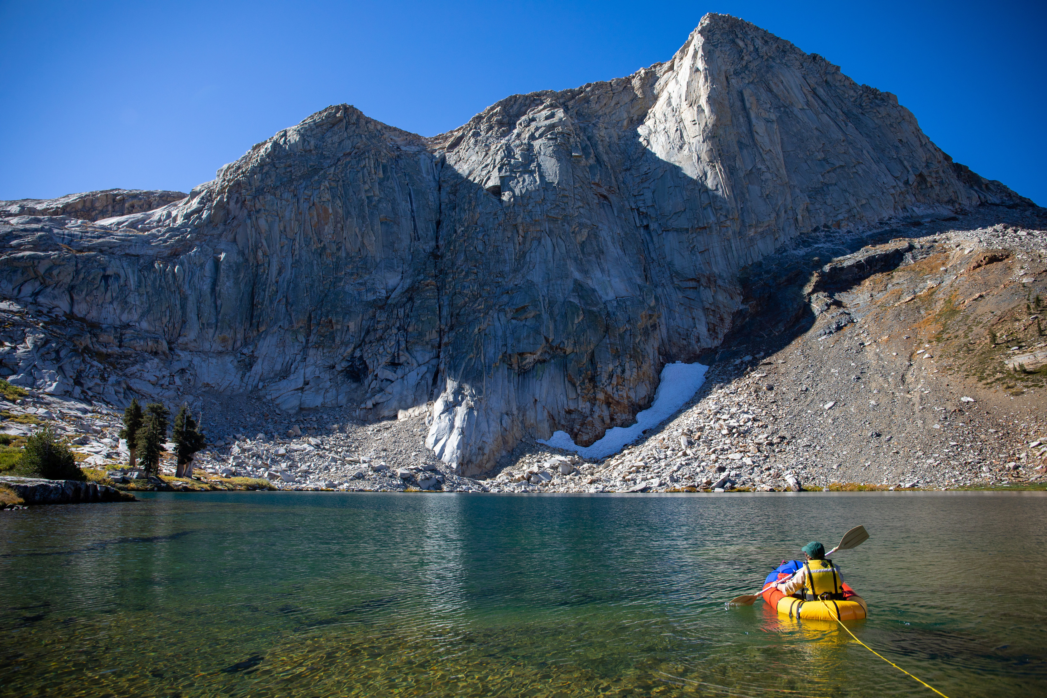 View of woman in raft paddling out into clear mountain lake with rugged mountains on opposite shore.