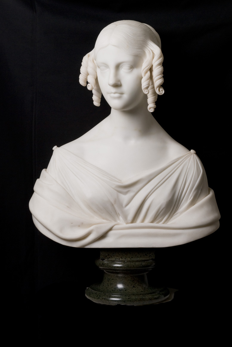 White bust of young woman with corkscrew curls and updo, wearing draped top with buttons at shoulders.