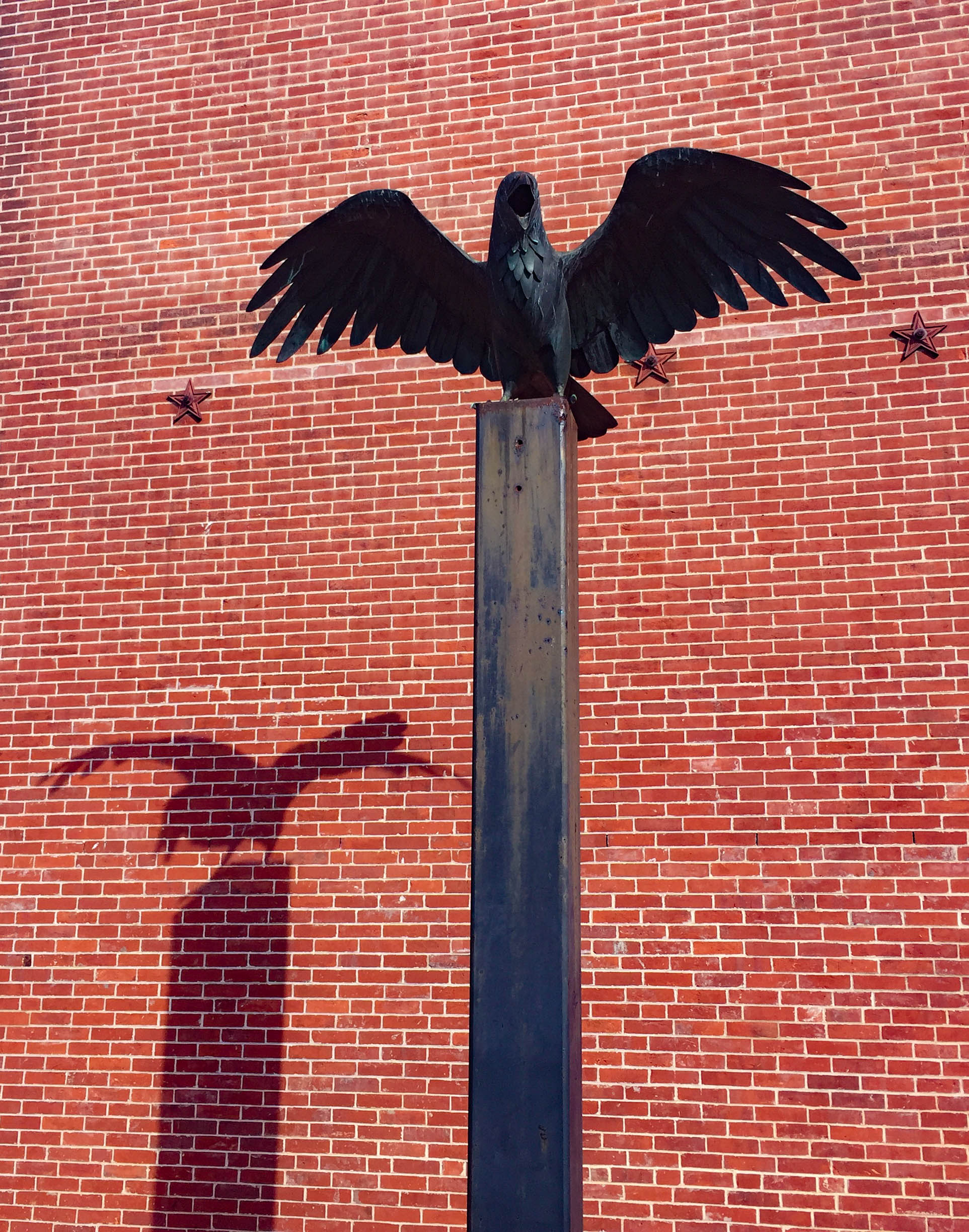 Statue of a raven spreading its wings outside of a brick building