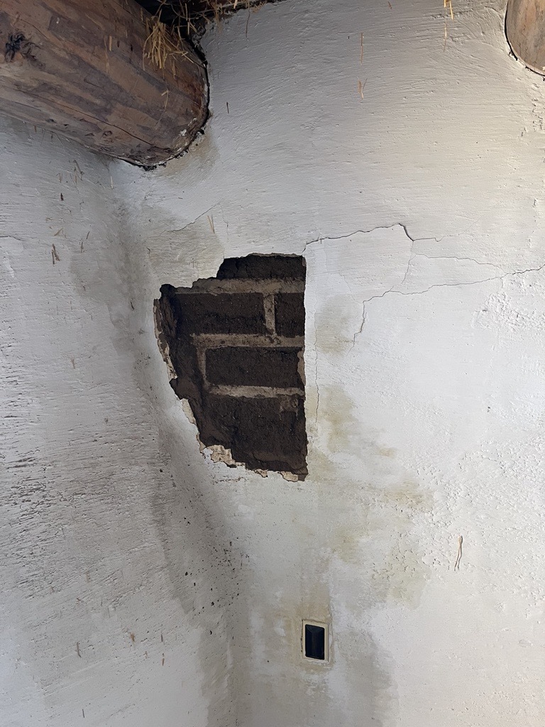 Amended adobe bricks are exposed through a section of white stucco that has fallen due to moisture exposure. 