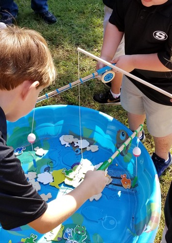 Children using toy fishing poles try to catch "fish" from a plastic pool. 