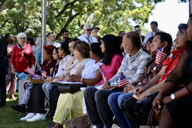 People sit under a tent holding American flags listening to a presentation