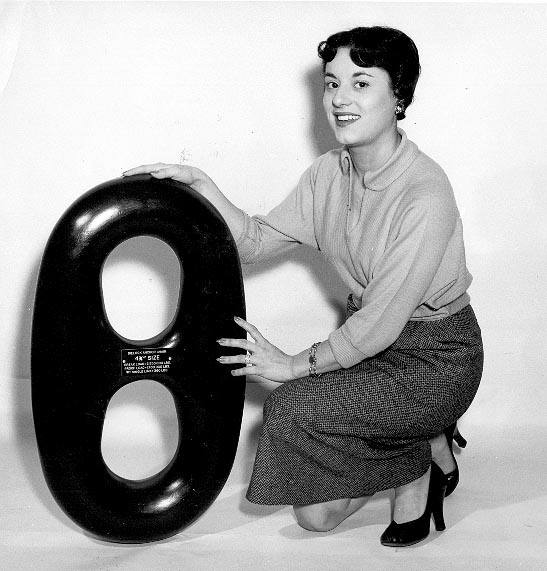 Woman in a skirt in blouse standing next to a large anchor chain link. 