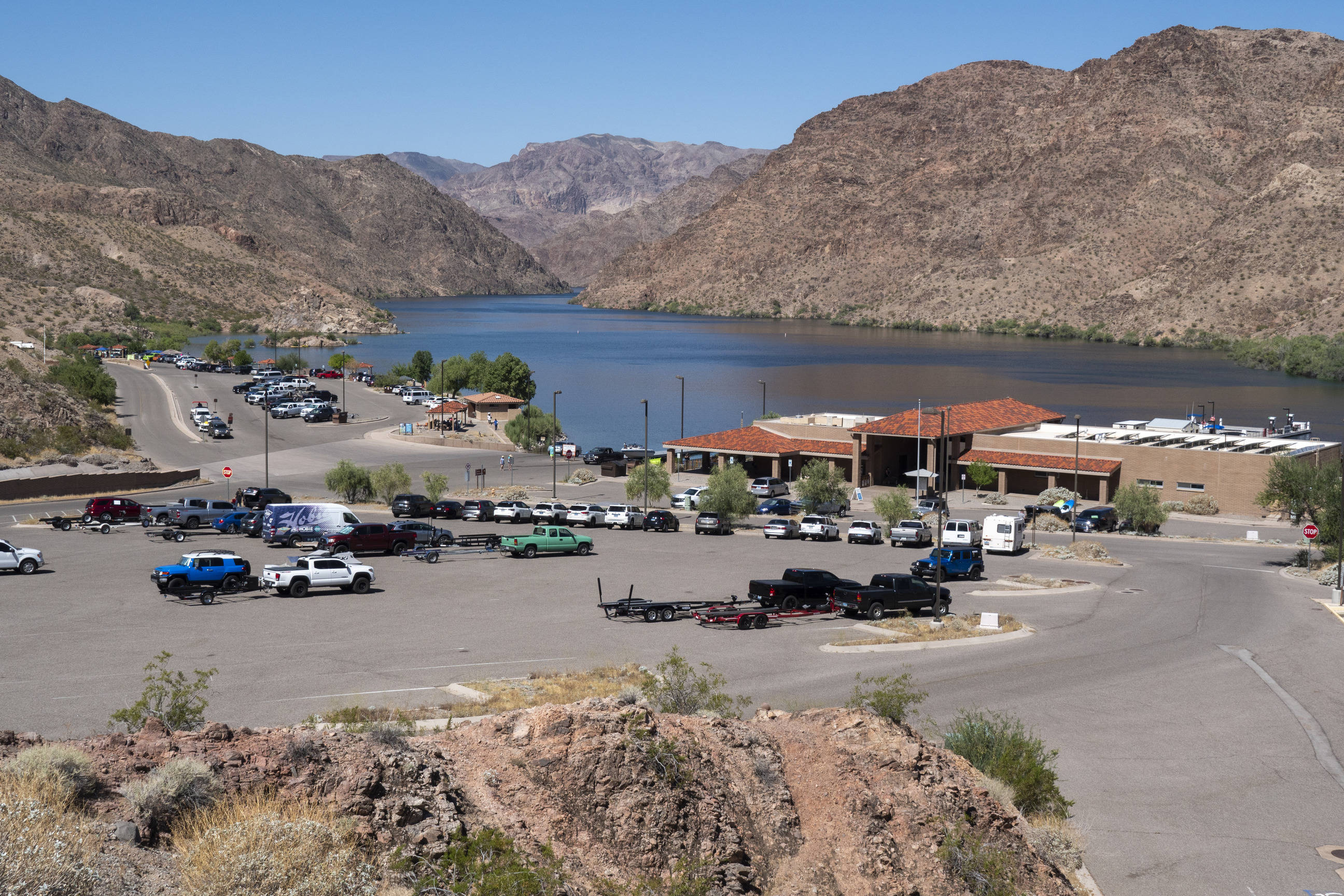 rock covered hill foreground, parking lot cars and building mid, river surrounded by tall desert hills background