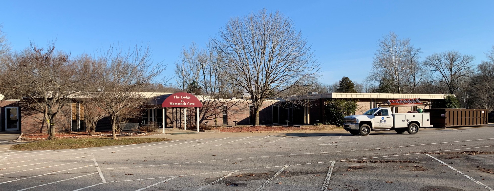 A long single-story brink building with a red awning that says “The Lodge at Mammoth Cave” under a blue sky.