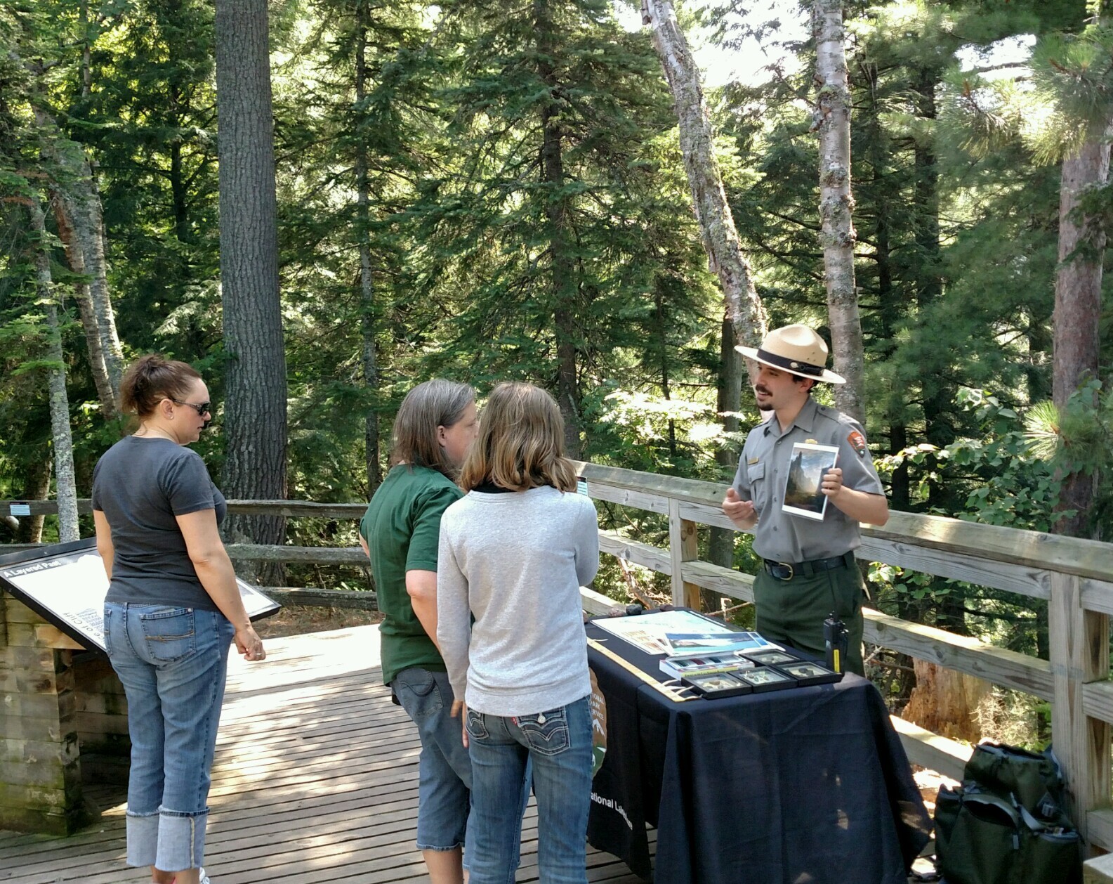 Park ranger standing in front of a table with rock specimens and showing a couple of visitors a picture.