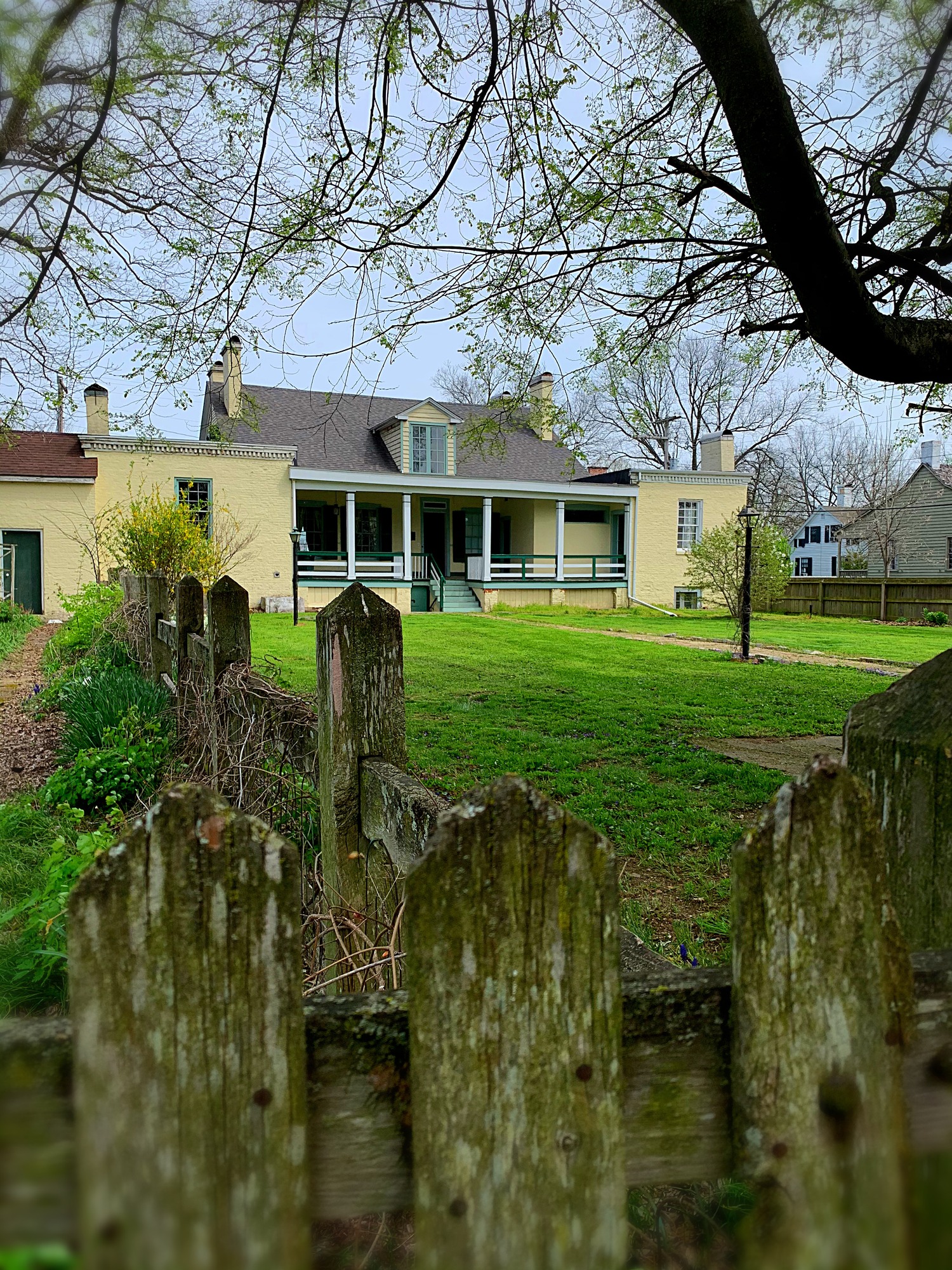wooden fence post with cream colored two-story frame house in the background and a yard between. 