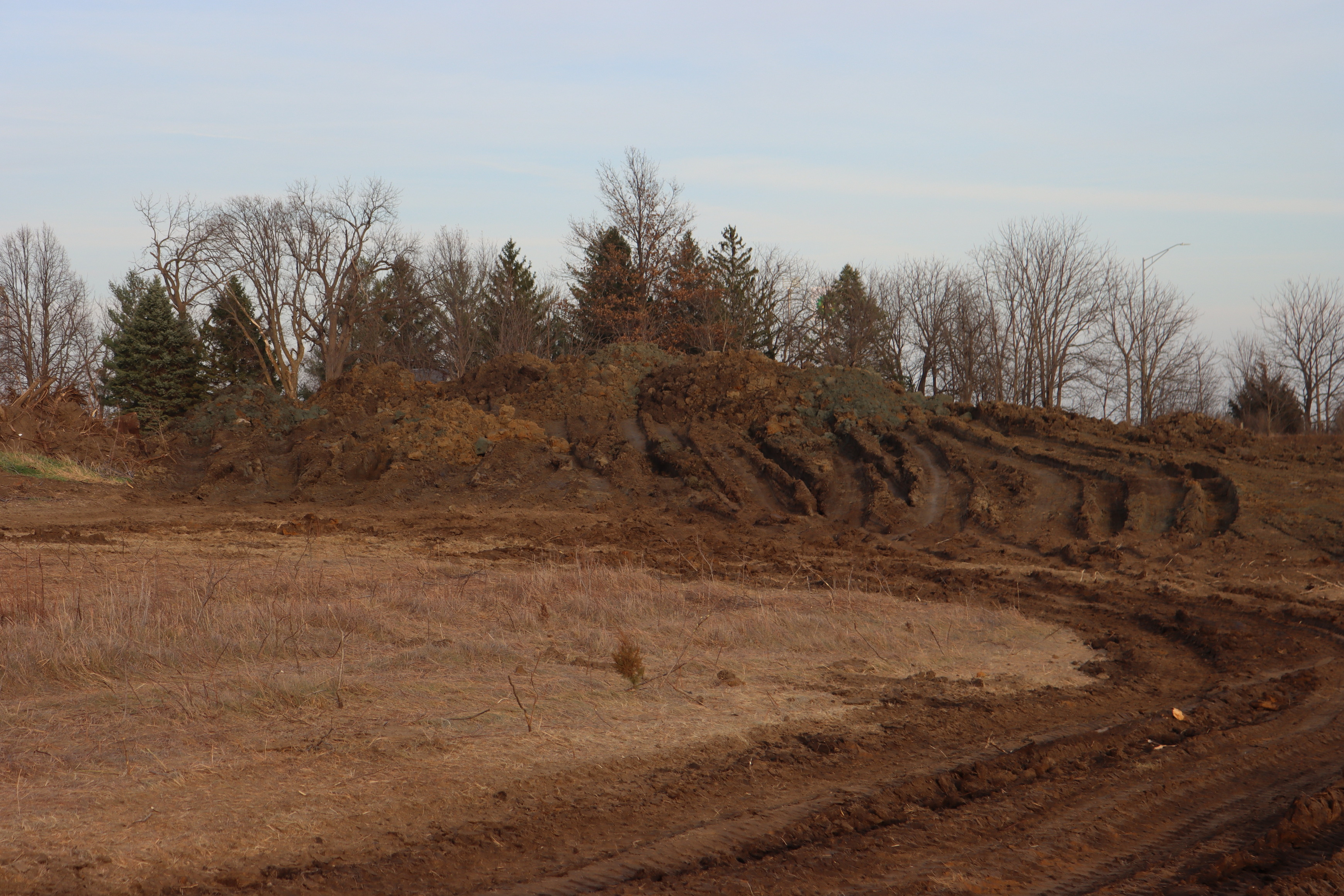 Large pile of dirt in center of image. Very deep tire tracks run up the side of the pile from dump trucks adding to berm.