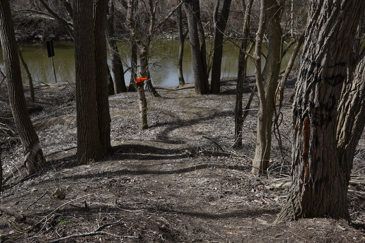 A dirt path slopes down through woods to the river.