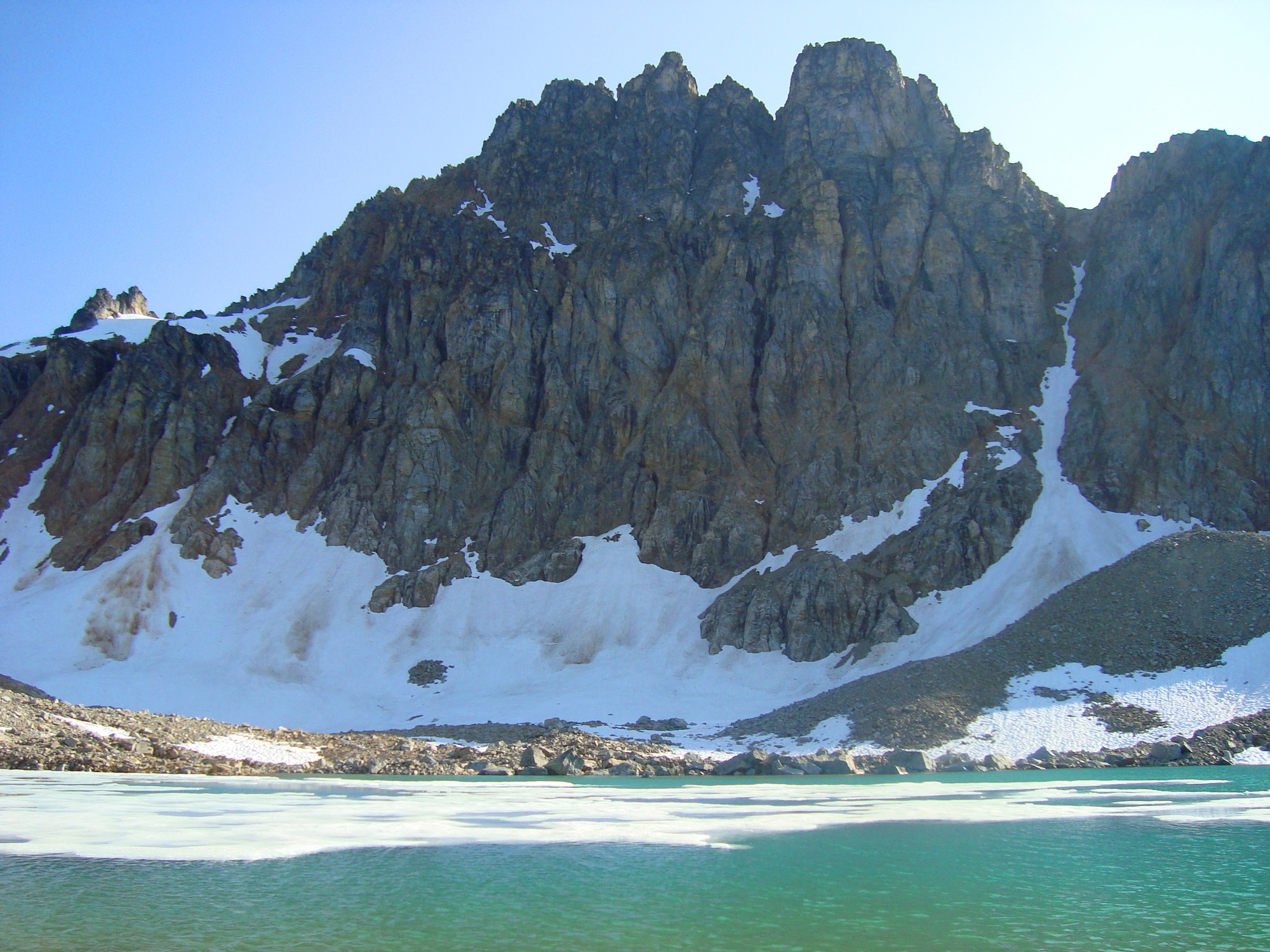 A turquoise lake with floating ice has the backdrop of a steep-cliffed gray-brown mountain.