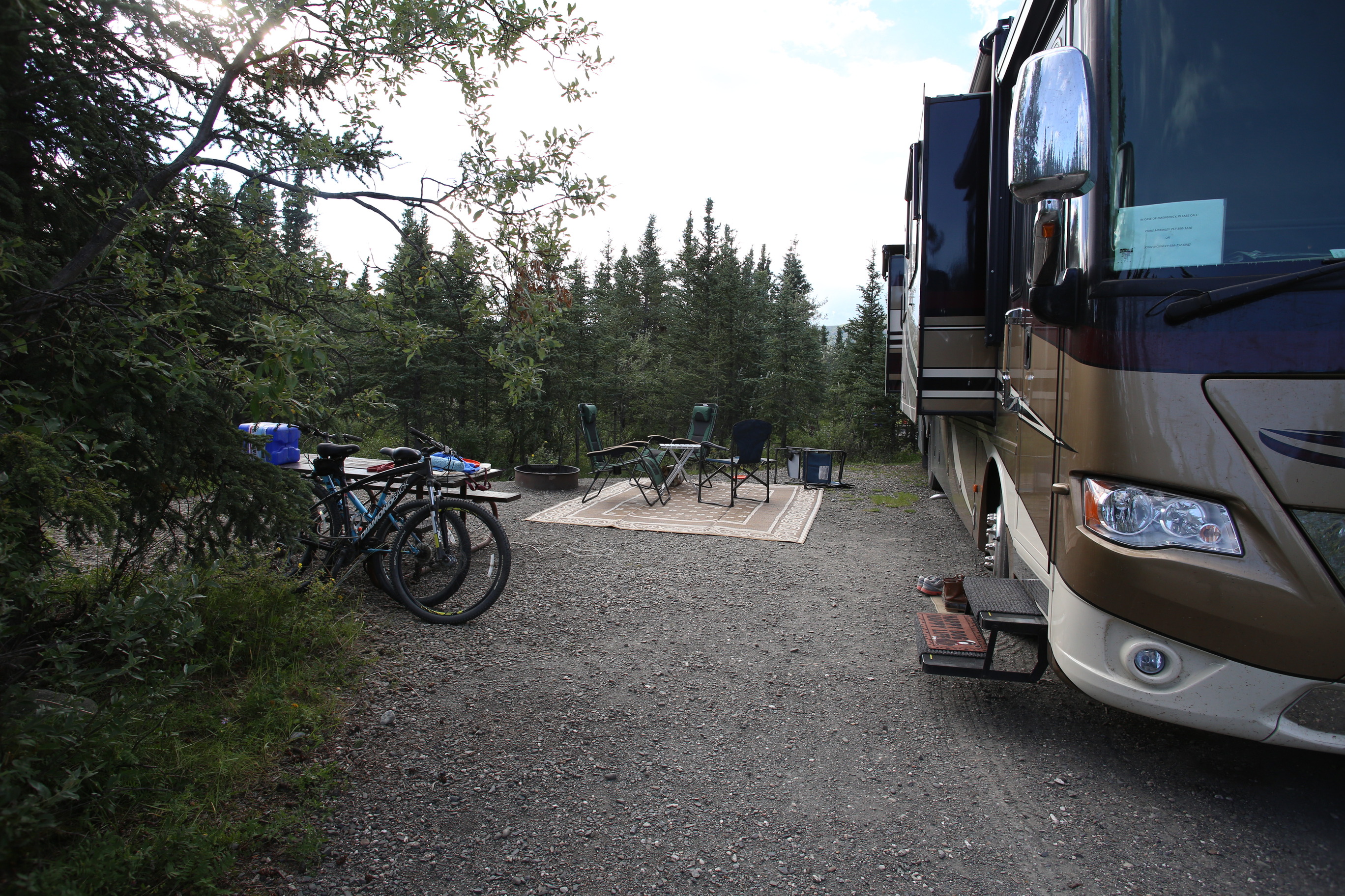 a large R V parked next to camp chairs and bicycles