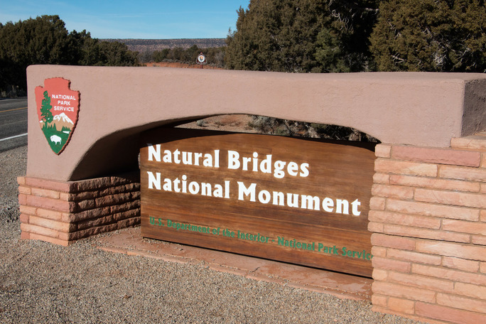 An entrance sign with the National Park Service Arrowhead and text Natural Bridges National Monument.