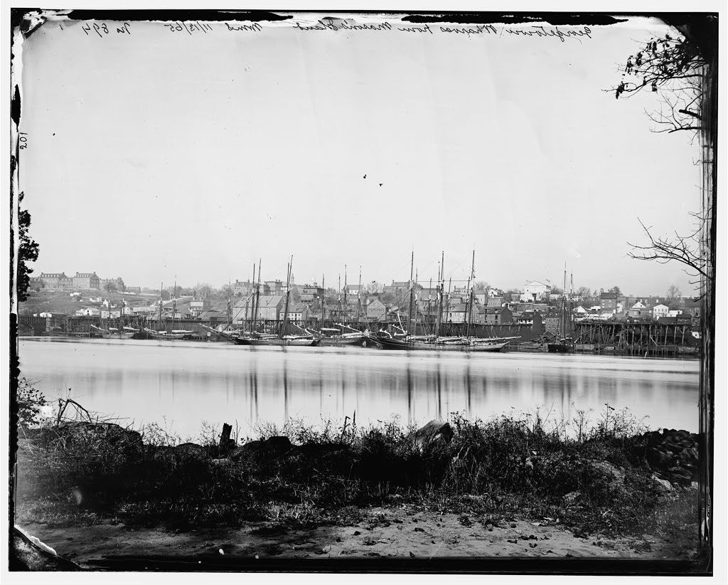 Historical black and white photo of sailing vessels in the distance docked at Georgetown, Washington, DC.