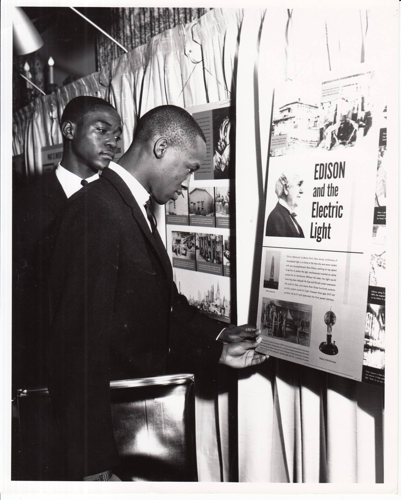 Visitors examining poster, "Edison and the Electric Light," at unidentified exhibition.
