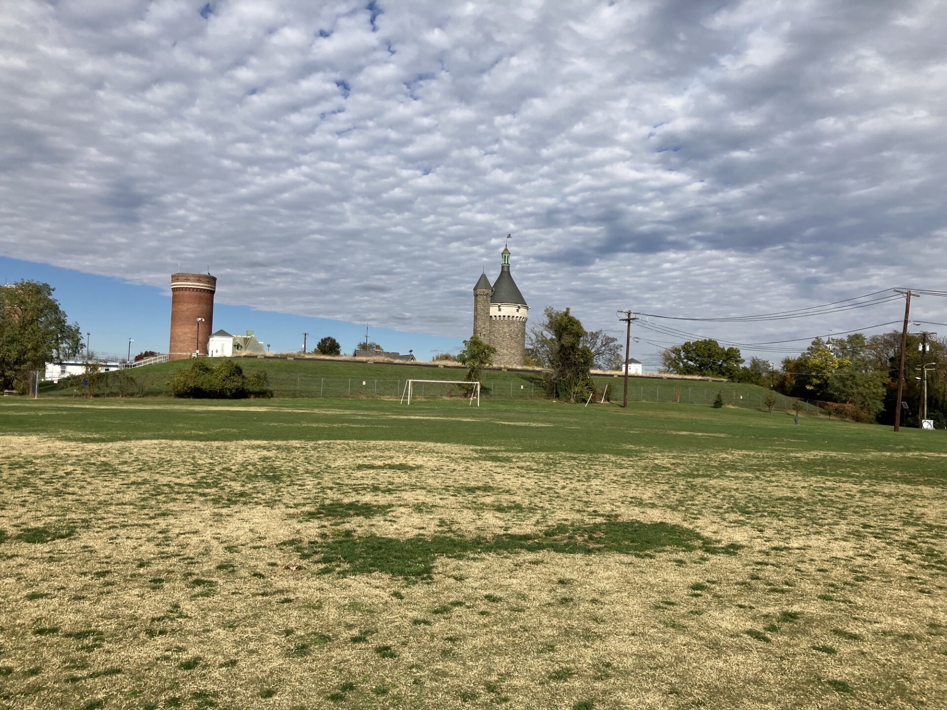 A grassy field leading to two tower structures on a cloudy day.