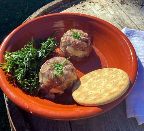 Orange dish with two jellied moose balls, a cracker, and some green carrot tops.