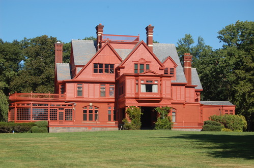 Large salmon colored mansion with several gabled roofs. 
