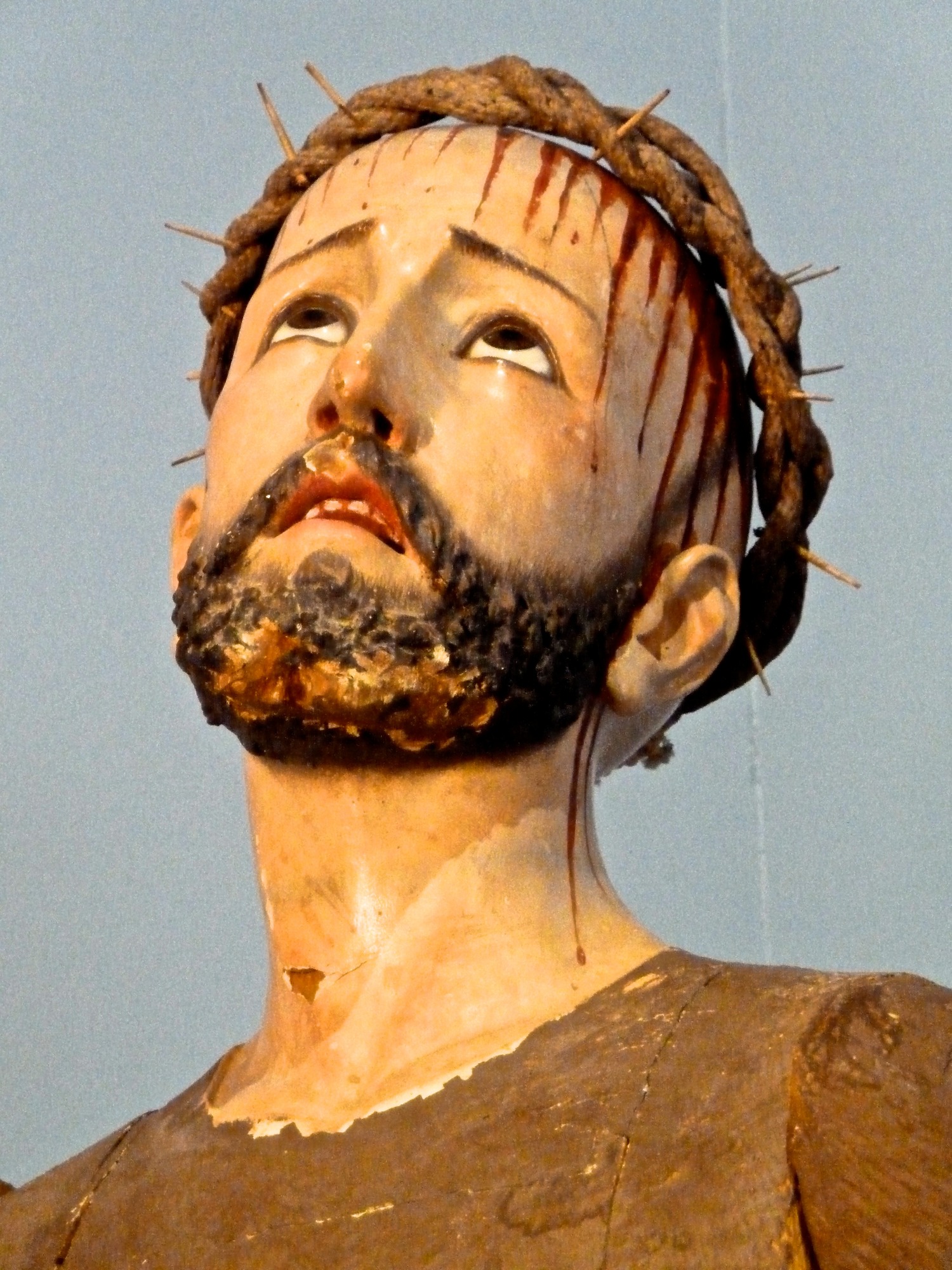 closeup of wooden carved statue head, with crown of thorns and blood