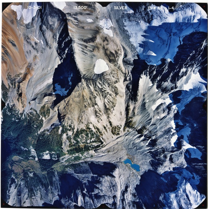 Color aerial photograph of glacier, snowfields and alpine lake on mountain peak.