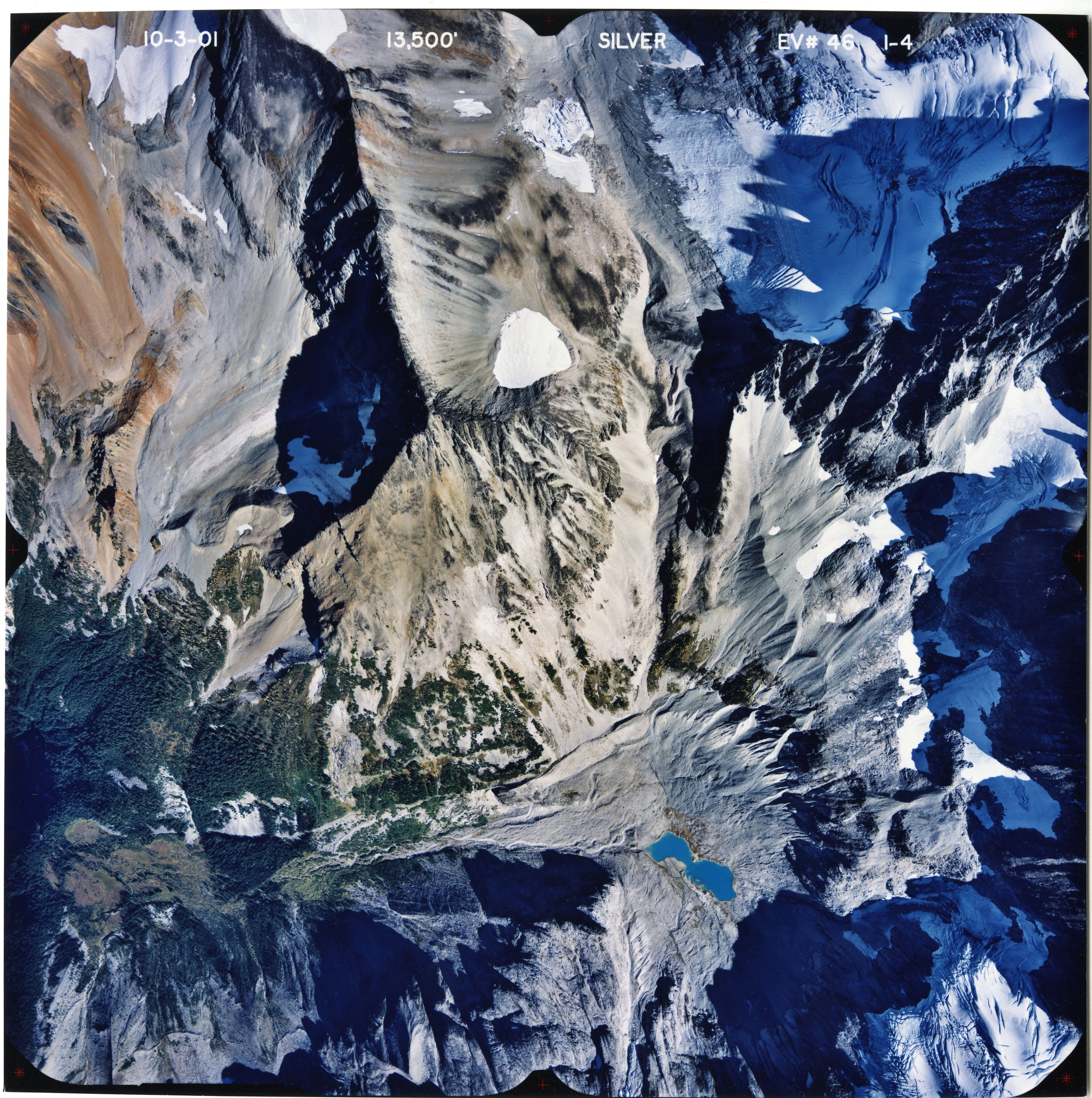 Color aerial photograph of glacier, snowfields and alpine lake on mountain peak.